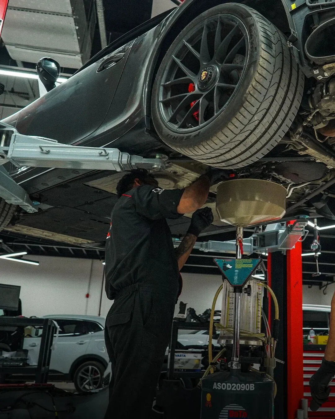 Technician working under a car on a lift in an auto repair shop